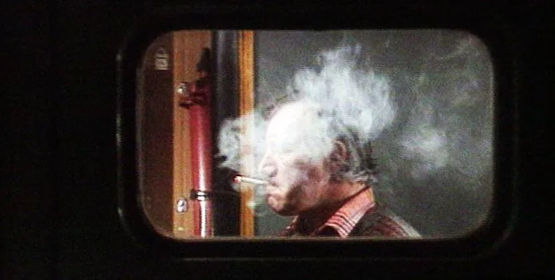 A man smoking, seen through the window of a compartment door
