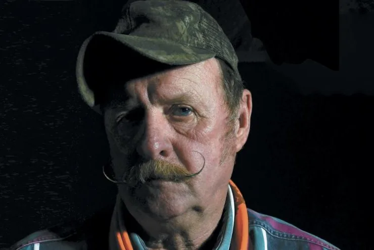 Portrait of a man with a curled moustache and a camouflage cap, half in shadow